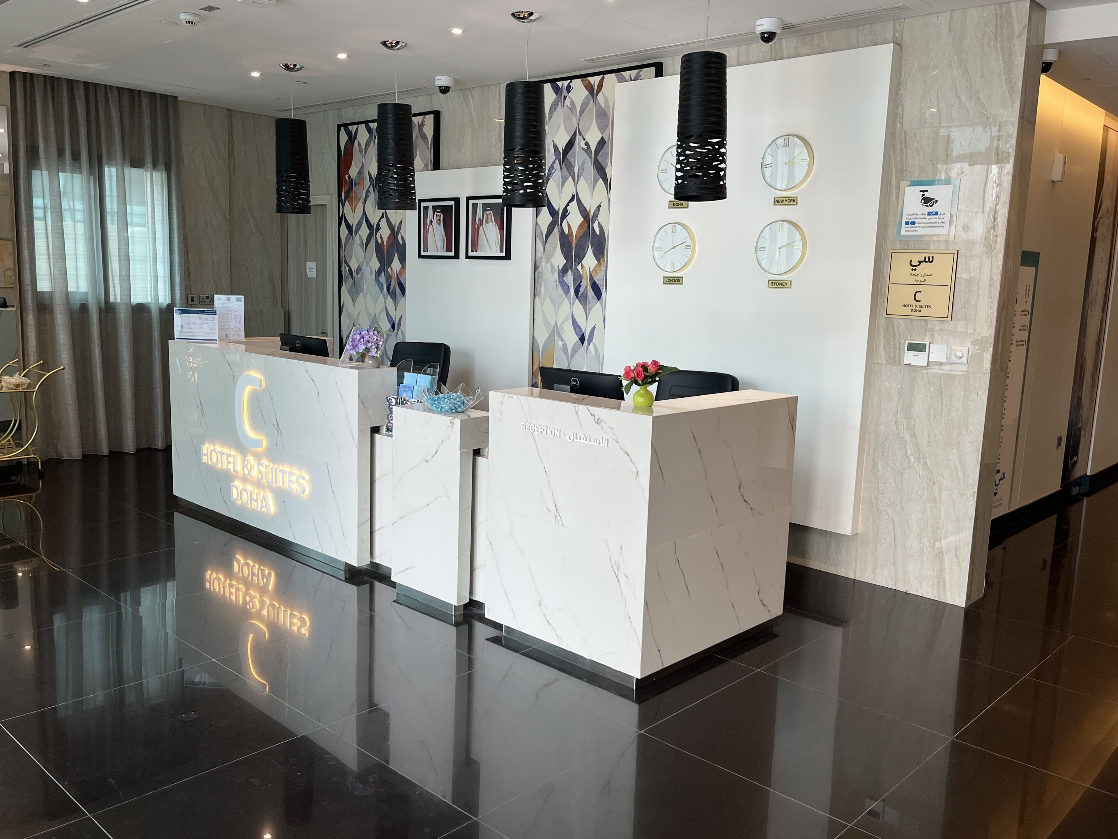 Zona de recepción de un hotel con mostradores de mármol, relojes mostrando la hora en varias ciudades y un diseño moderno y limpio.