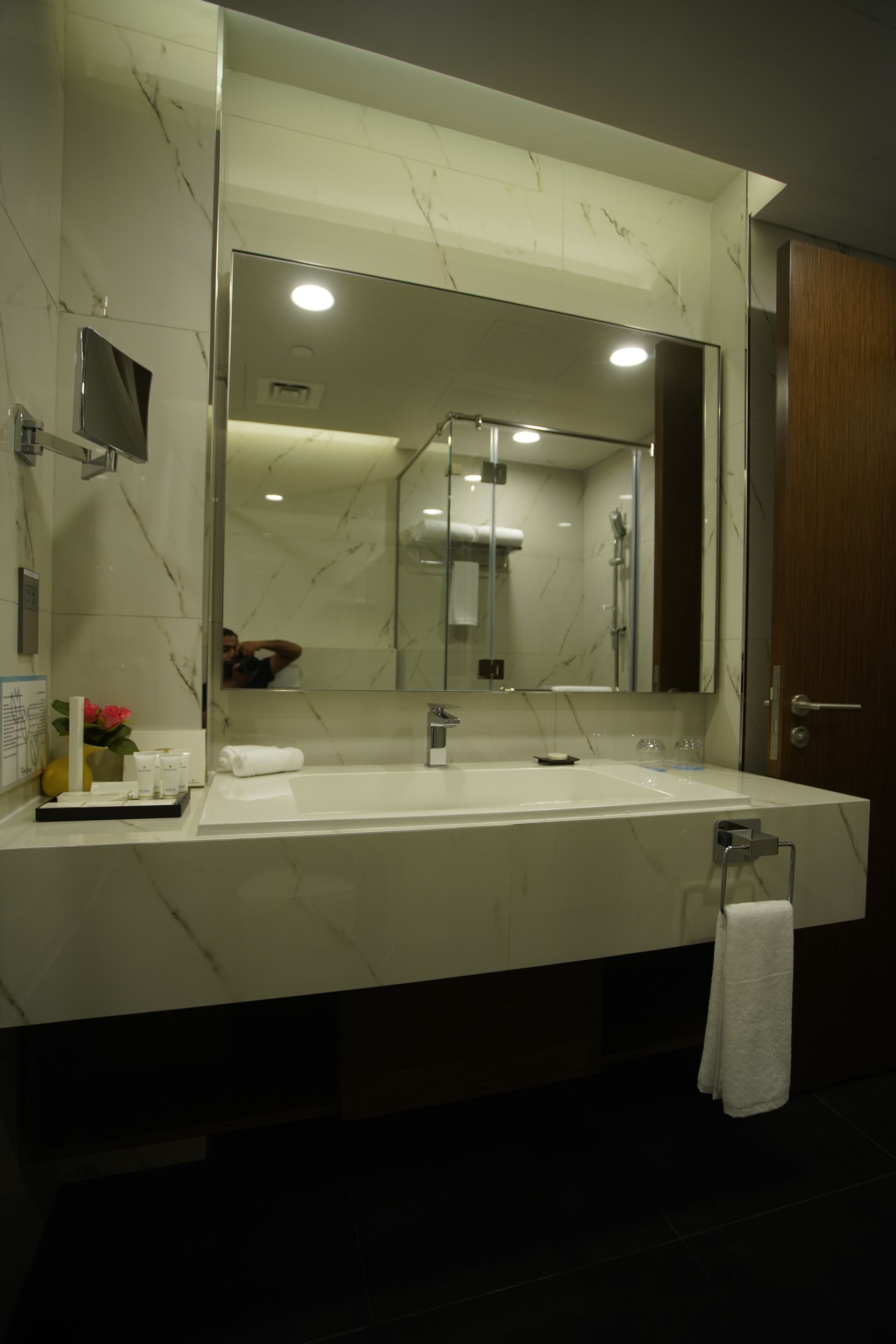 A modern bathroom with a large mirror, a white sink, and a towel rack.