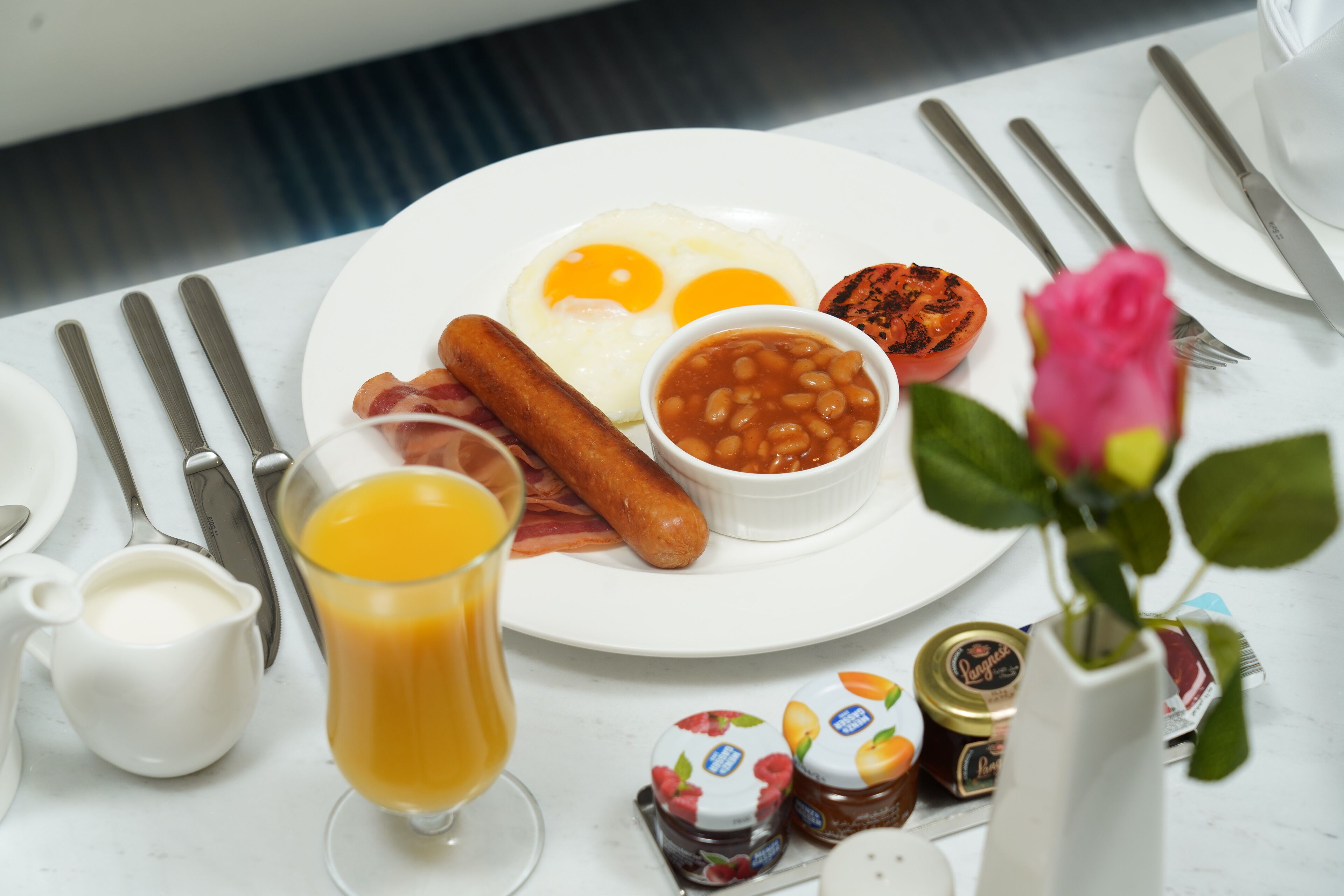 A breakfast plate with eggs, sausages, beans, and a glass of orange juice.