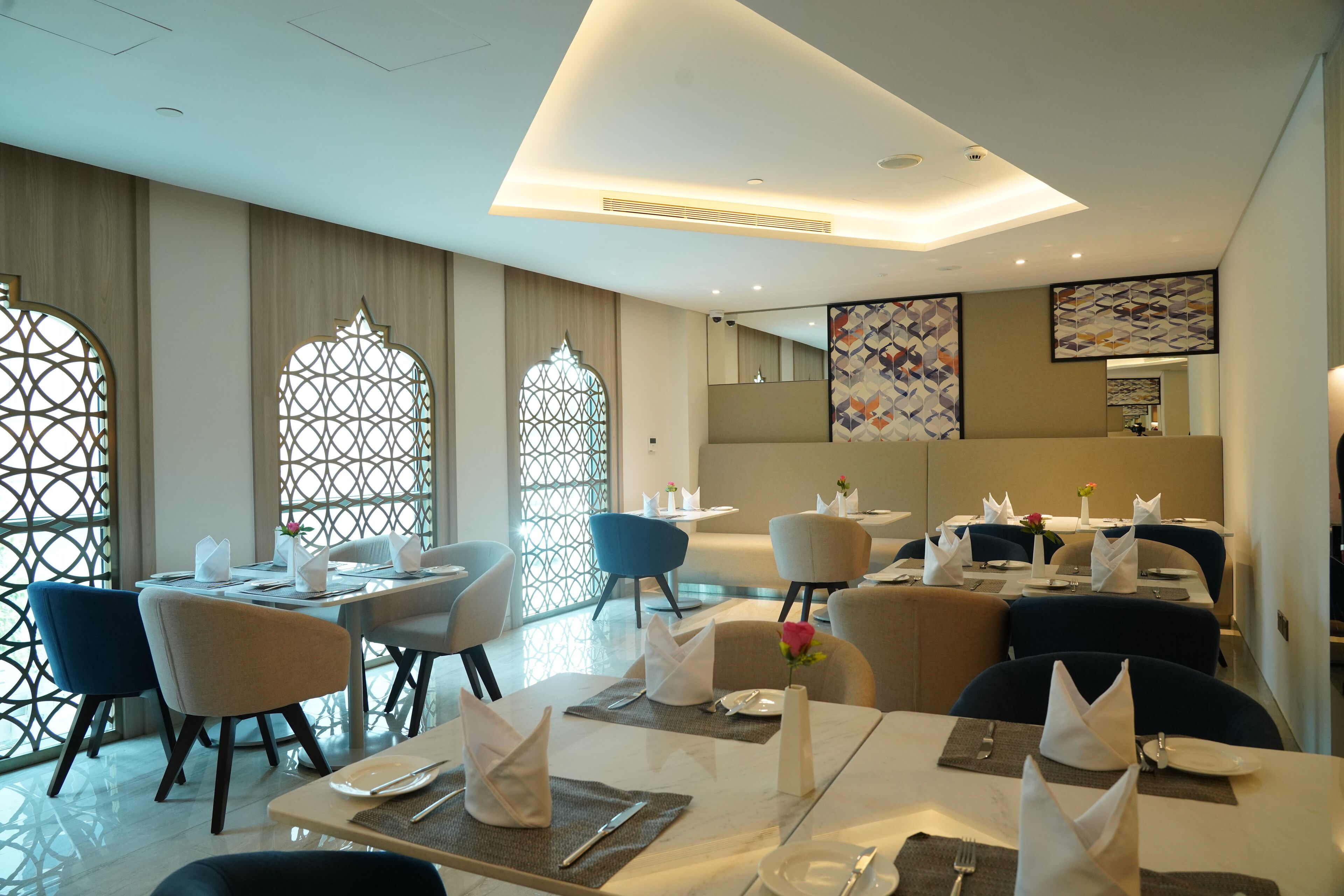 A modern dining area with tables set for service, featuring geometric patterned windows and contemporary furniture.