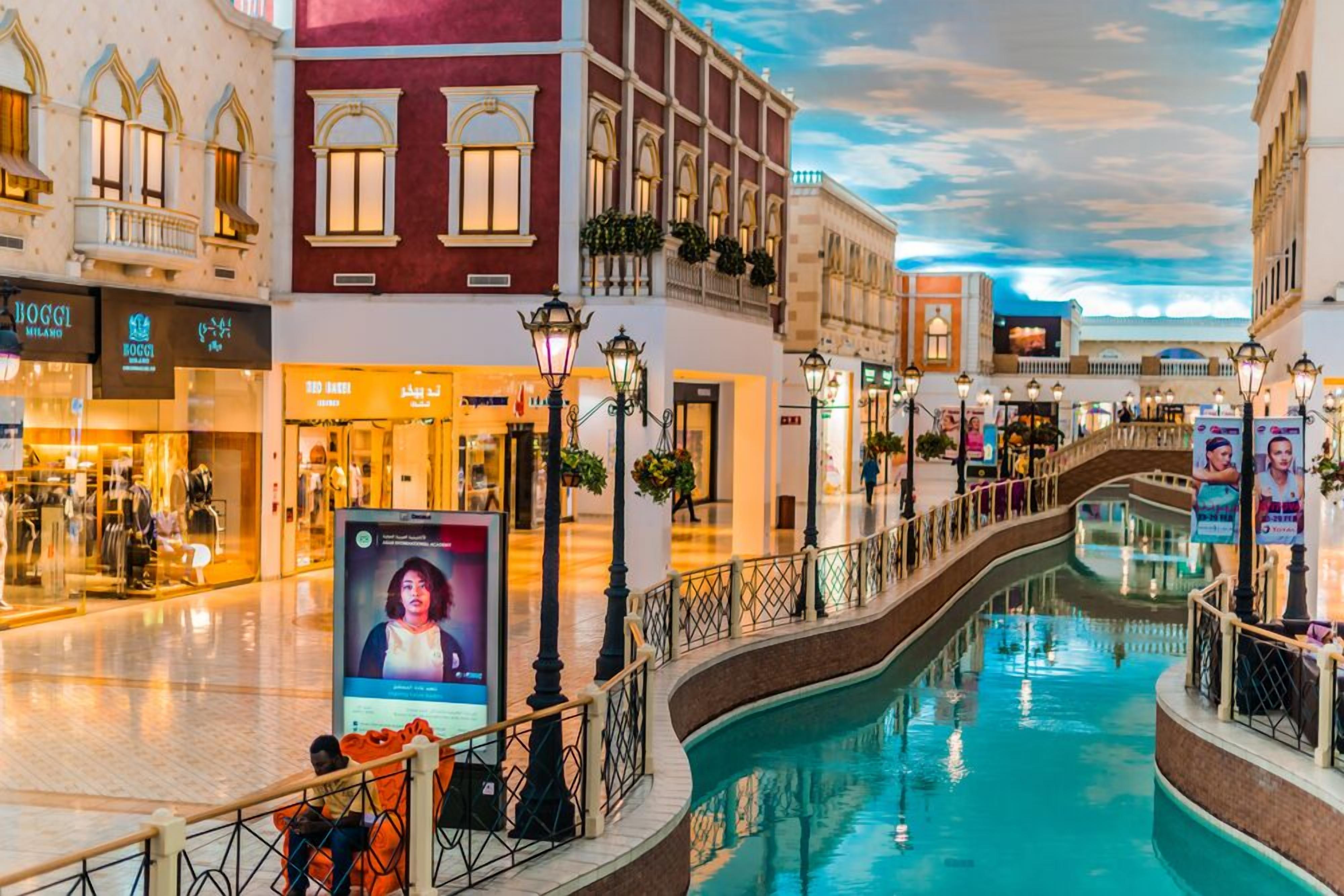 Un centro comercial con una fuente central, tiendas y un puente peatonal.