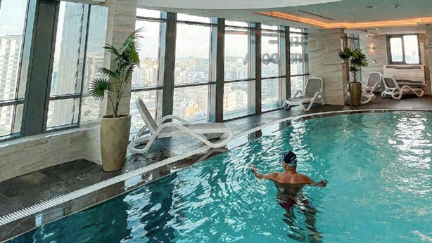Una piscina interior con techo de cristal, amplias ventanas y sillones de descanso.