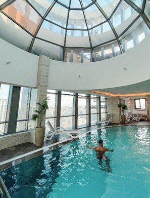 Una piscina interior con techo de cristal, amplias ventanas y sillones de descanso.