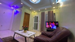 Una sala de estar con televisor, un sillón de cuero marrón, una mesa de centro blanca y una lámpara de techo.