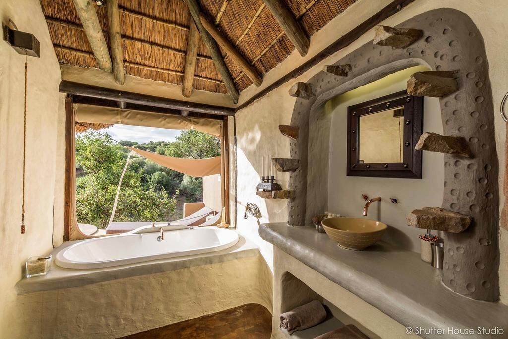 A bathroom with a large bathtub, a sink with a bowl, a mirror, and a window with a view of greenery.