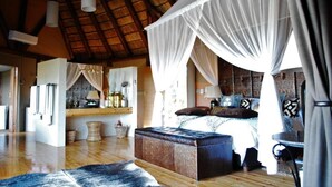 Um quarto espaçoso com uma cama grande, um dossel, piso de madeira e teto rústico.