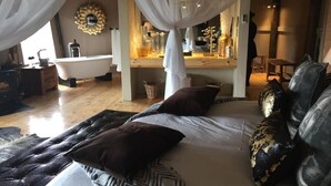 Quarto com uma cama grande, banheira e toucador com espelhos e artigos de higiene.