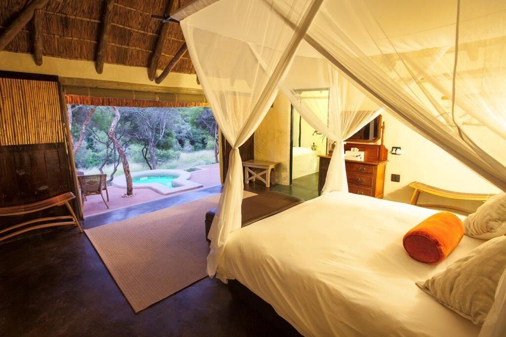 A bedroom with a bed, a nightstand, a chair, a wooden cabinet, and a view of an outdoor area with a pool and trees.