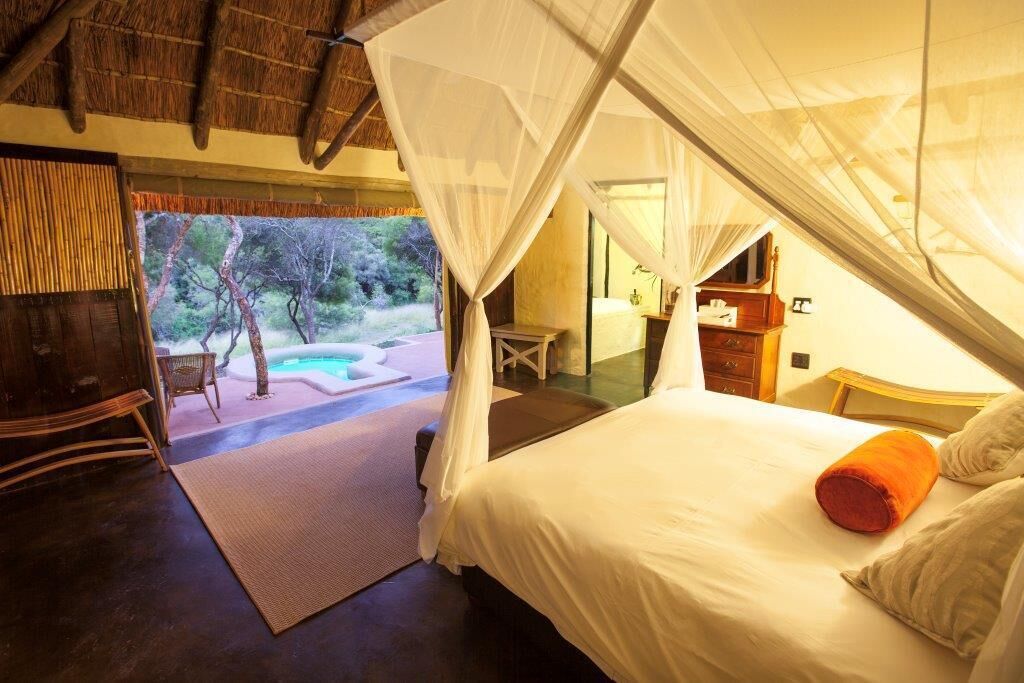 A bedroom with a bed, a nightstand, a chair, and a view of a pool and trees.
