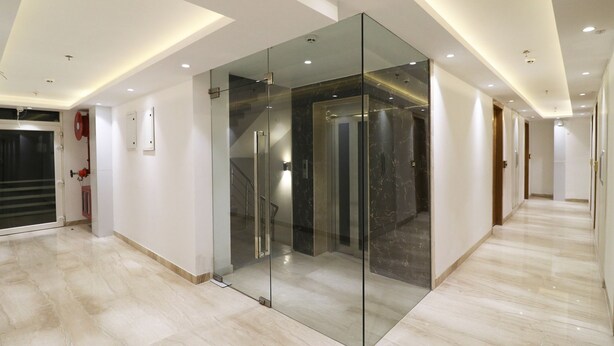 Een moderne hal met een glazen lift, marmeren vloer en inbouwverlichting.