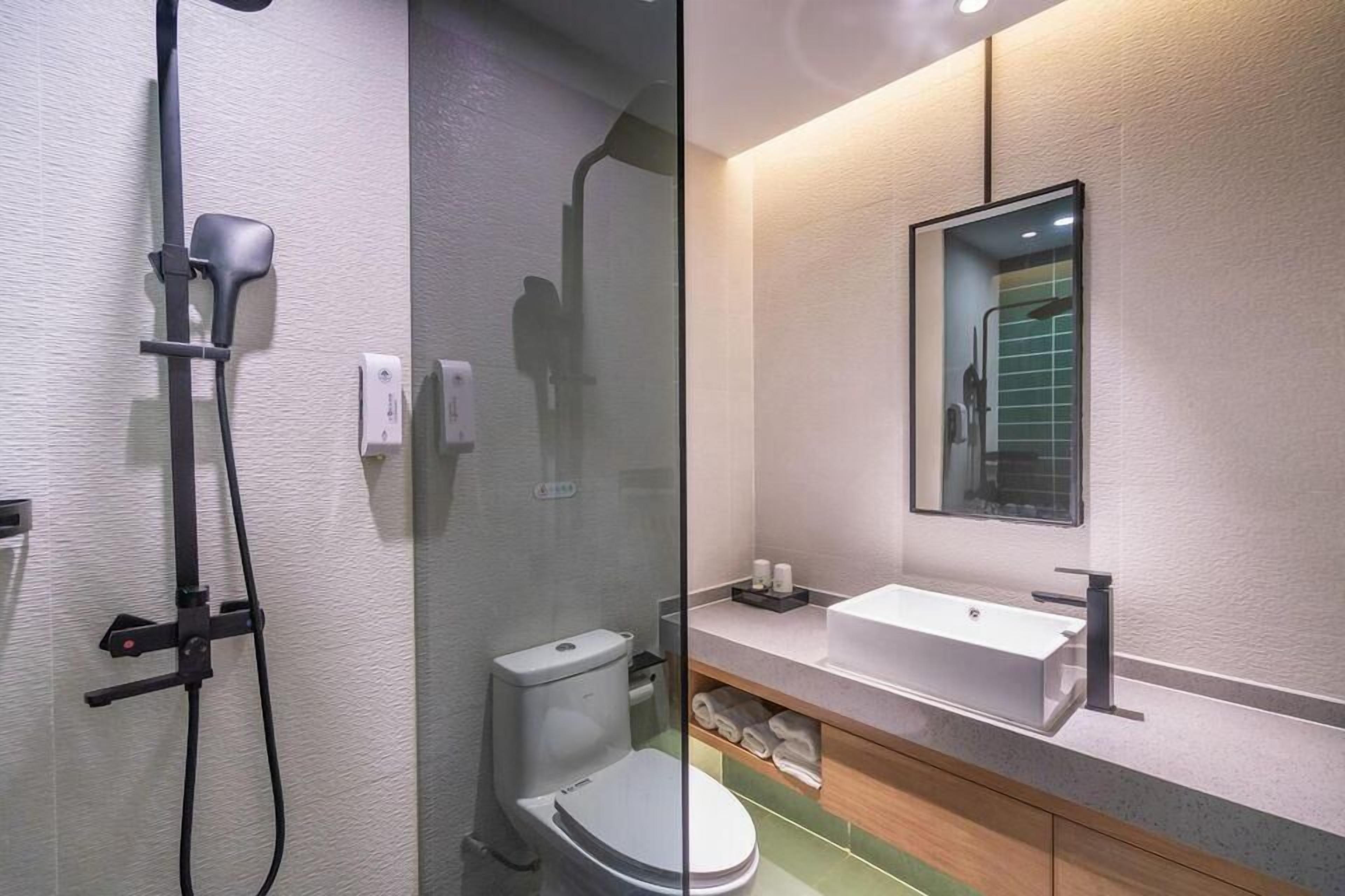 A modern bathroom with a glass shower enclosure, a toilet, a sink with a mirror above it, and a towel rack.