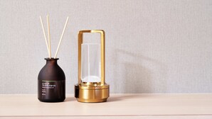 A dark brown bottle with wooden sticks and a golden glass container on a wooden surface against a plain wall. - Boxi Hakata 1 -Sleep Hotel- (Fukuoka)