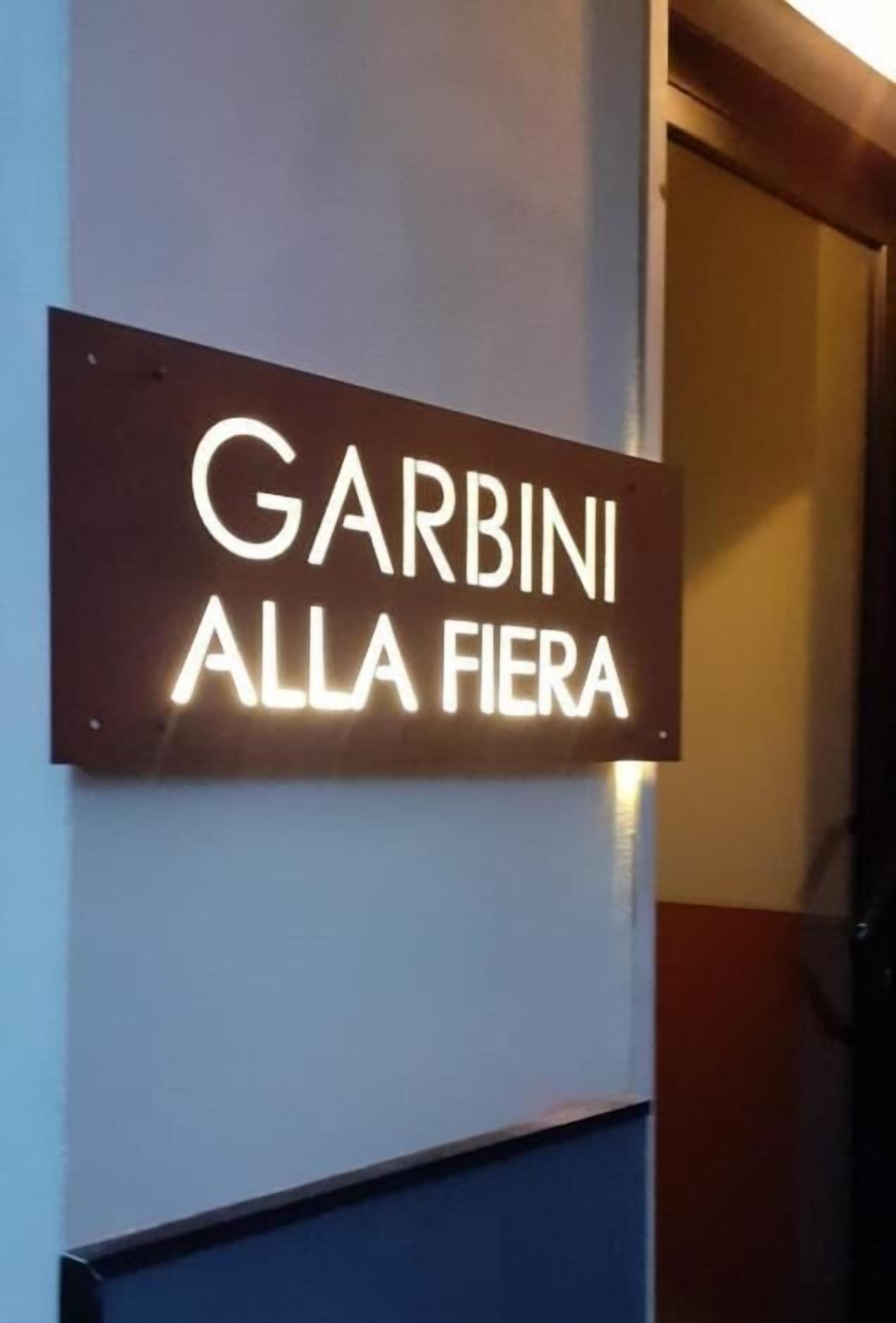 Ein Schild mit der Aufschrift 'GARBINI ALLA FIERA' an einer Wand.