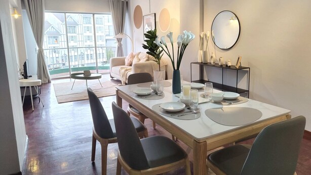 Un comedor moderno con una mesa grande dispuesta para cuatro personas, rodeada de sillas. Se ve un sofá y una pequeña mesa redonda al fondo.
