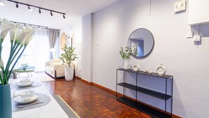 Una habitación de hotel moderna con suelo de madera, una mesa de comedor blanca con platos y cubiertos, una consola negra con adornos y un espejo grande en la pared.