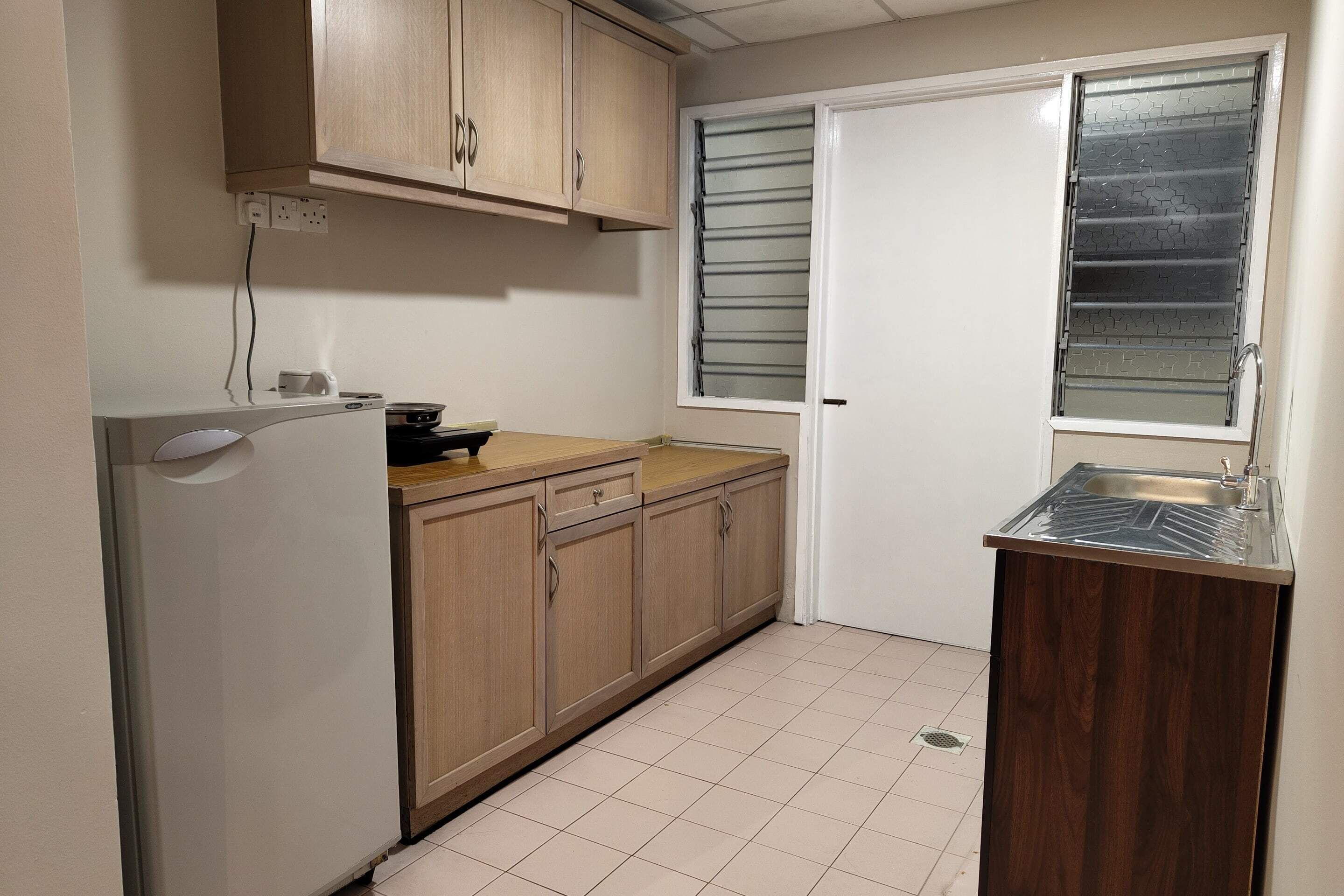 A small kitchen with wooden cabinets, a white refrigerator, a sink, and a window with a metal grill.