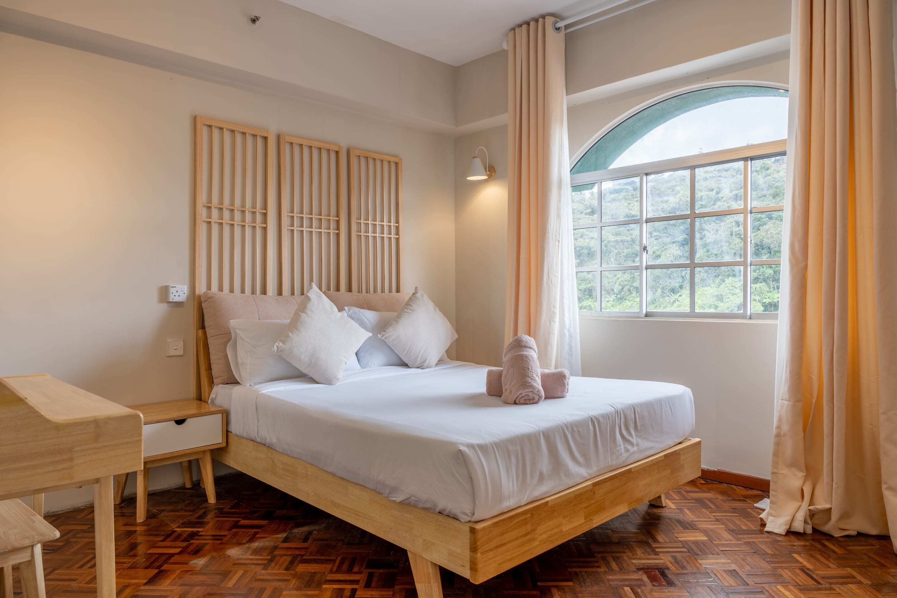 Une chambre à coucher avec un lit en bois, une table de chevet, un bureau et une fenêtre avec des rideaux.