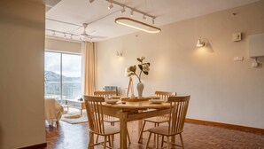 Comedor con mesa y sillas de madera, un jarrón con flores y vistas al exterior a través de ventanas amplias.