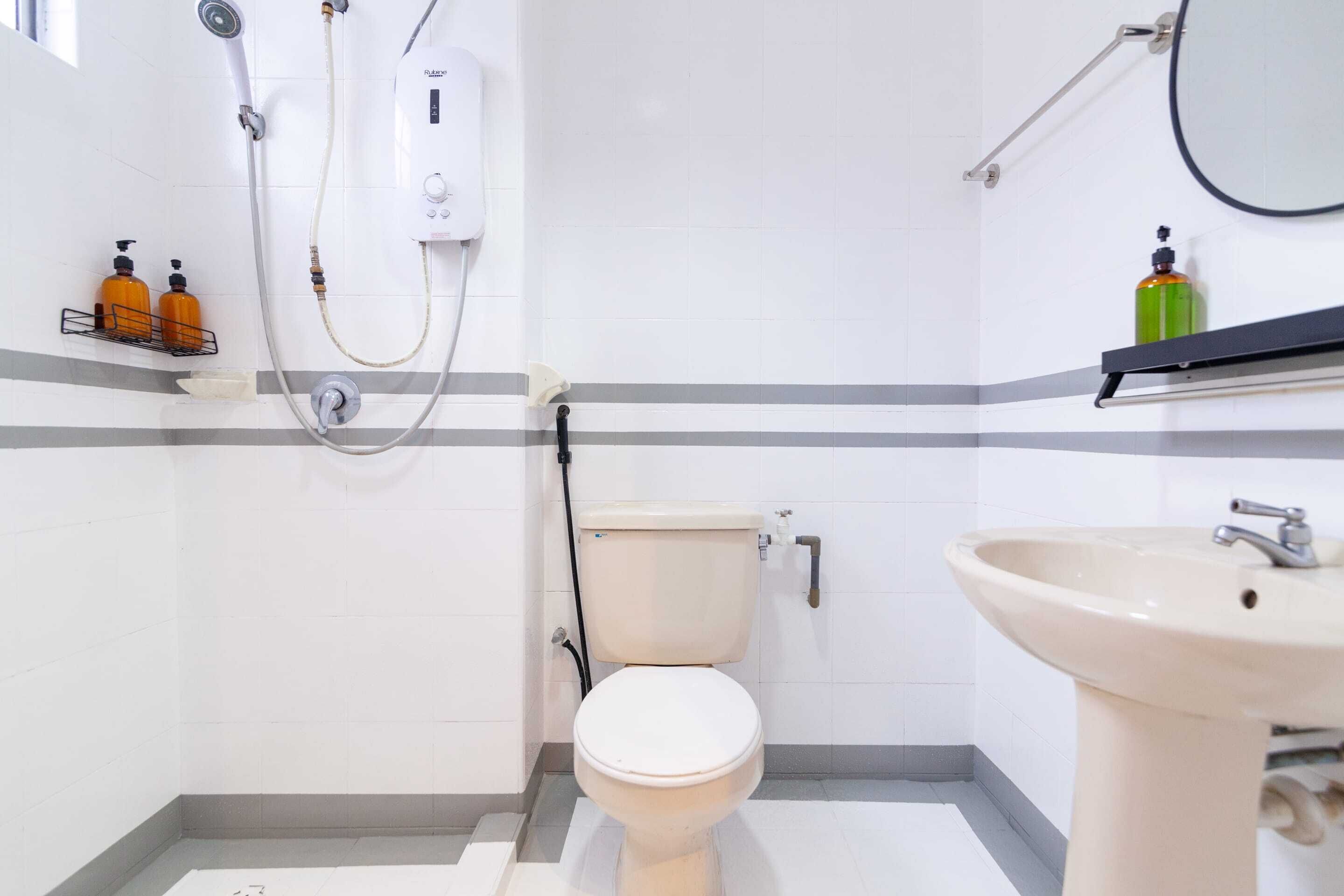 Ein Badezimmer mit Toilette, Waschbecken und Dusche. An einem Regal befinden sich Seifenspender und über dem Waschbecken ein Spiegel.