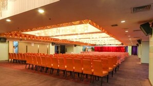 A conference room with rows of orange chairs, a carpeted floor, and a stage with a red curtain. - Star Hotel (Guangzhou)