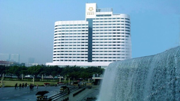 A modern hotel with a prominent logo on the top, surrounded by a public square with a large water feature. - Star Hotel (Guangzhou)
