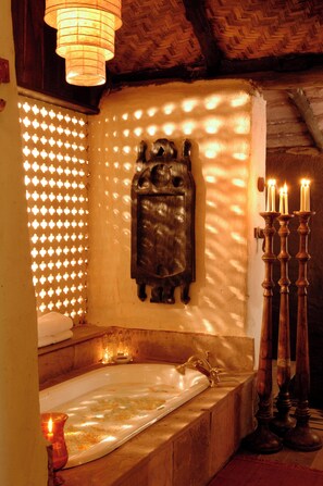 A bathroom with a bathtub, a wooden wall decoration, and a row of candles. - Mahua Kothi (Manpur)