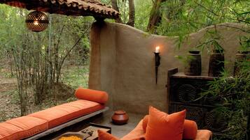 An outdoor seating area with a sofa and a table, surrounded by greenery and a stone wall.
