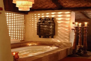 A bathroom with a bathtub, a wall-mounted decorative piece, a candle holder, and a patterned window. - Mahua Kothi (Manpur)