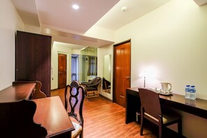 A hotel room with a wooden dining table, two chairs, a desk with a lamp, and a water bottle on the desk. - Myspace Hotel At Bgc (Taguig)