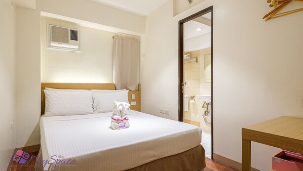 Habitación de hotel con cama, mesita de noche, espejo y baño visible a través de una puerta abierta.