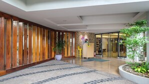 Un vestíbulo de hotel con un mostrador de recepción de madera, una planta en maceta y un suelo de baldosas.