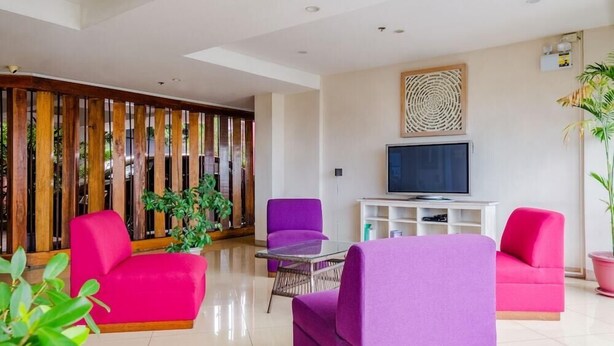 A modern living room with a TV, purple and pink sofas, a glass coffee table, and a wooden partition with vertical slats. - Myspace Hotel At Bgc (Taguig)