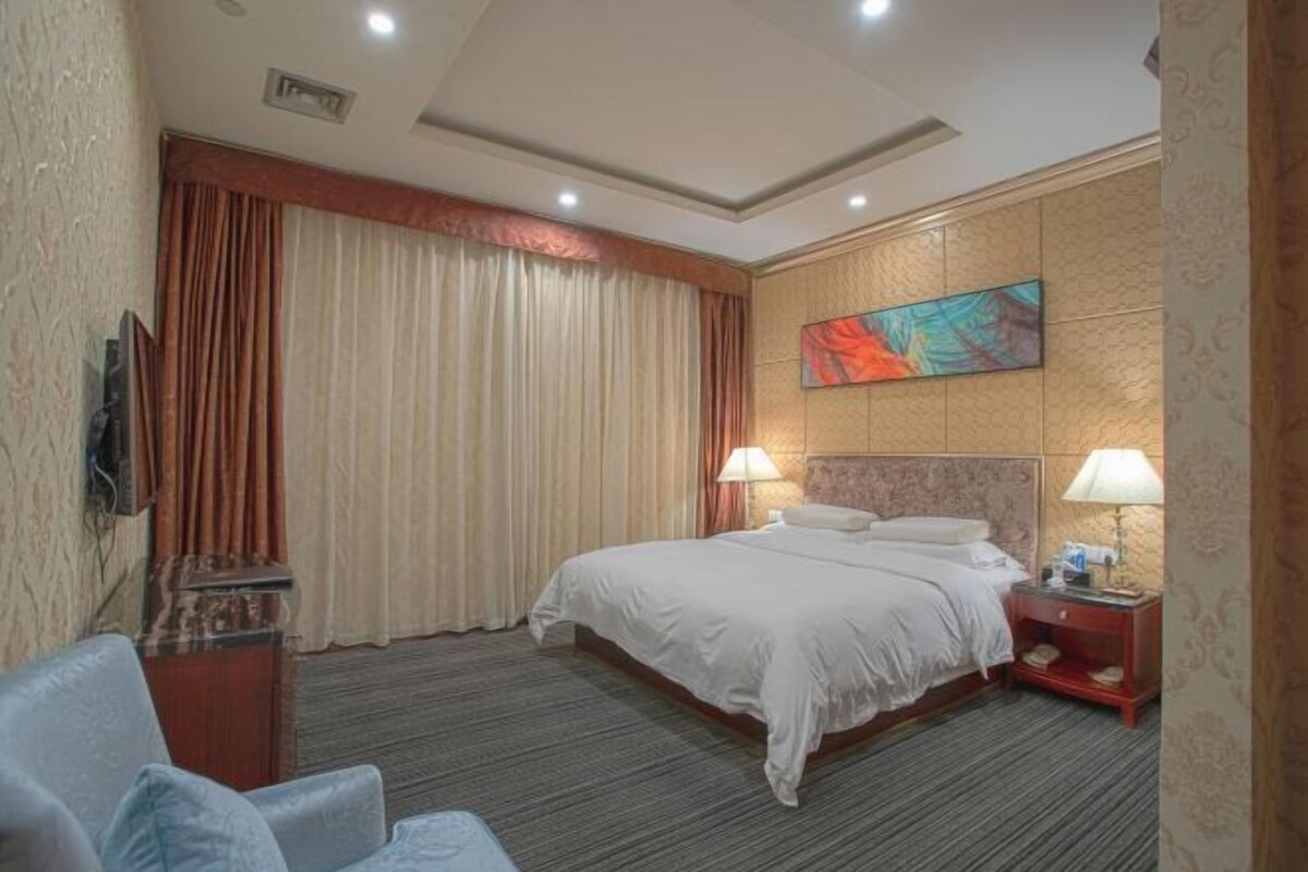 Una habitación de hotel con una cama, dos lámparas de noche, un televisor y un cuadro en la pared.