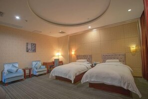 Habitación de hotel con dos camas, dos sillones, una mesita y un cuadro en la pared.