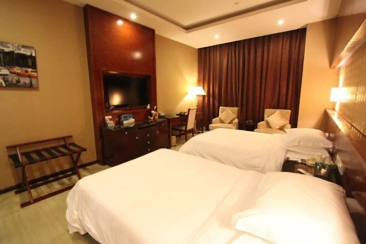 A hotel room with two beds, a TV, a desk, a chair, and a lamp.