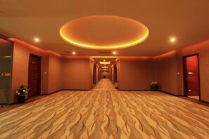 Un couloir d’hôtel avec un tapis à motifs, des portes des deux côtés et un luminaire circulaire au plafond.