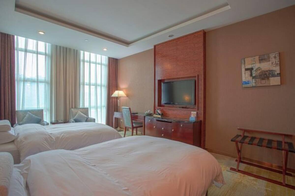 A hotel room with two beds, a desk, a television, and a window with curtains.
