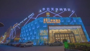Un hotel con fachada moderna, señalización iluminada y un estacionamiento.