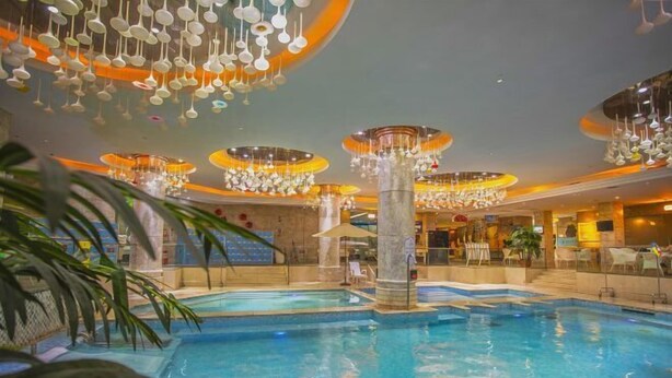 Una piscina interior con varios niveles de asientos alrededor de todo el borde, rodeada de candelabros modernos y una columna central.