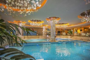 Ein Innenpool mit mehreren Sitzebenen entlang des Randes, umgeben von modernen Kronleuchtern und einer zentralen Säule.