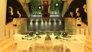Un moderno vestíbulo de hotel con una pared de vidrio, sillas blancas, una escalera central y una pared decorativa con motivos florales.