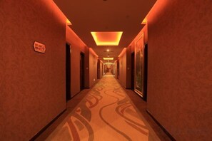 Un pasillo de hotel con suelo alfombrado, puertas a ambos lados y un cartel en la pared izquierda.