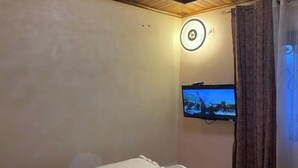 Una camera d'albergo con un letto, una TV a parete, un lampadario circolare e una tenda.