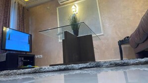 Un soggiorno moderno con una TV a schermo piatto, un tavolino da caffè con piano in vetro, una pianta in vaso e un divano.