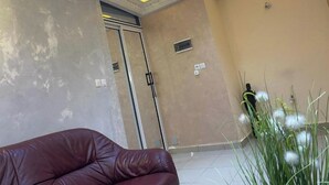 Una stanza con un divano in pelle marrone, una porta scorrevole, una piccola pianta e un soffitto decorato con illuminazione a incasso.
