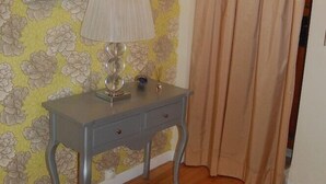 Une pièce avec un plancher en bois, une console grise surmontée d’une lampe, un miroir et un rideau beige.