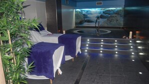 Une salle de spa équipée de deux tables de massage, d’un jacuzzi et d’une fresque représentant une cascade.