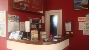 A reception desk with a red wall, framed artwork, informational posters, and a window. - Hotel Costa Cantabra (Argonos)