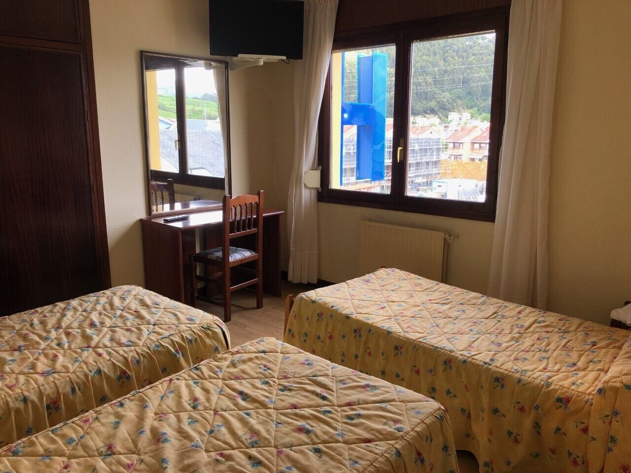 Une chambre avec deux lits, un bureau et une chaise. Il y a une fenêtre donnant sur des bâtiments et de la verdure.