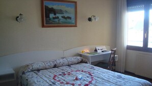 A bedroom with a bed, a nightstand, a painting, and a window with curtains. - Hotel Costa Cantabra (Argonos)
